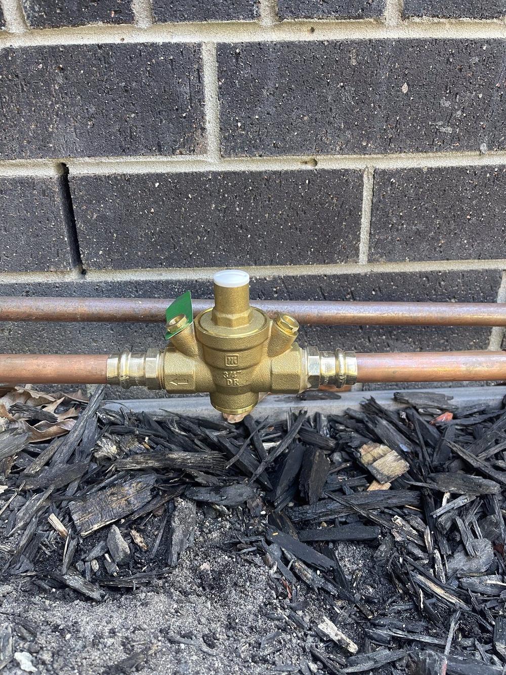 Brass pressure reducing valve fitted to copper supply line in garden mulch Brighton